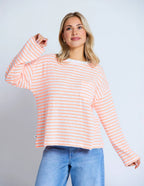 Woman wearing a pink and white striped sweater with blue jeans on a light gray background